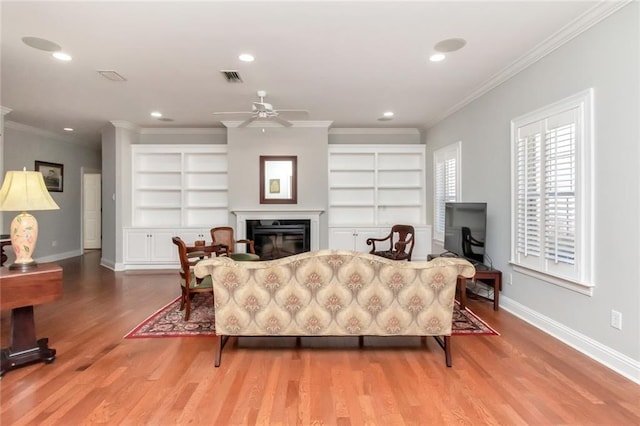 living area featuring a glass covered fireplace, visible vents, baseboards, and wood finished floors