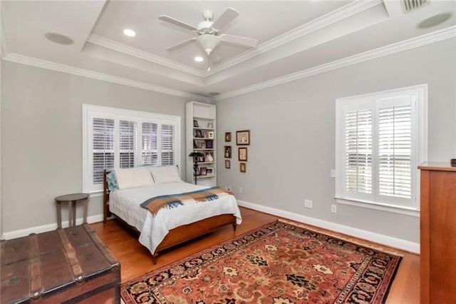 bedroom with a tray ceiling, wood finished floors, and baseboards