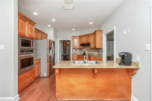 kitchen with a breakfast bar, stainless steel appliances, a sink, a peninsula, and under cabinet range hood