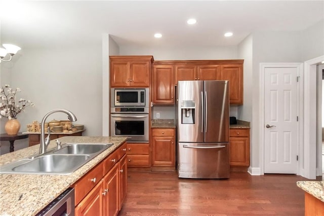 kitchen with light stone counters, appliances with stainless steel finishes, dark wood-type flooring, and a sink