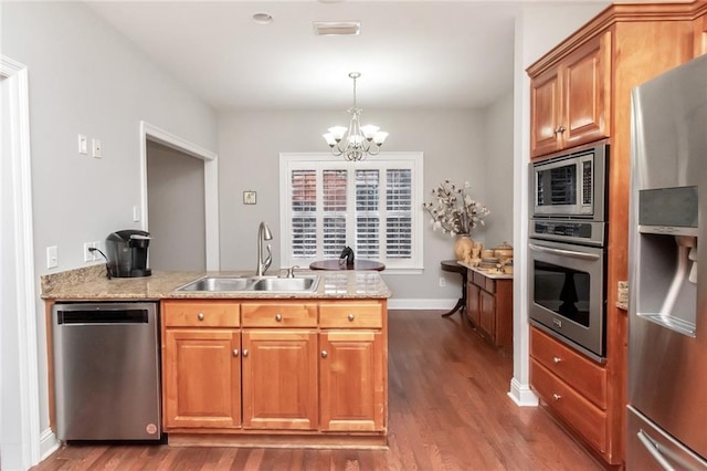 kitchen with brown cabinetry, dark wood-style flooring, stainless steel appliances, pendant lighting, and a sink