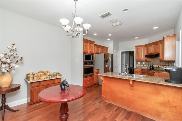 kitchen with stainless steel appliances, light countertops, under cabinet range hood, pendant lighting, and a sink