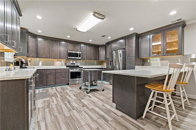 kitchen with dark brown cabinetry, light hardwood / wood-style floors, appliances with stainless steel finishes, and a breakfast bar