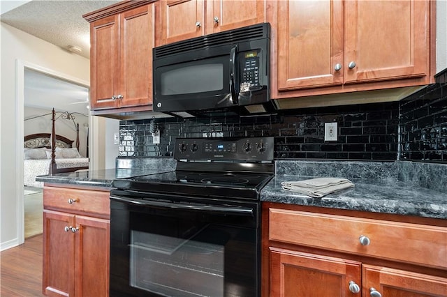 kitchen with hardwood / wood-style floors, black appliances, dark stone counters, and a textured ceiling