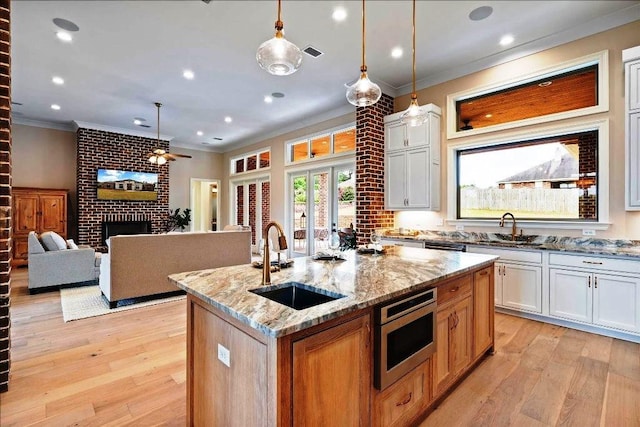 kitchen featuring white cabinetry, a center island with sink, light stone counters, a fireplace, and light wood-type flooring