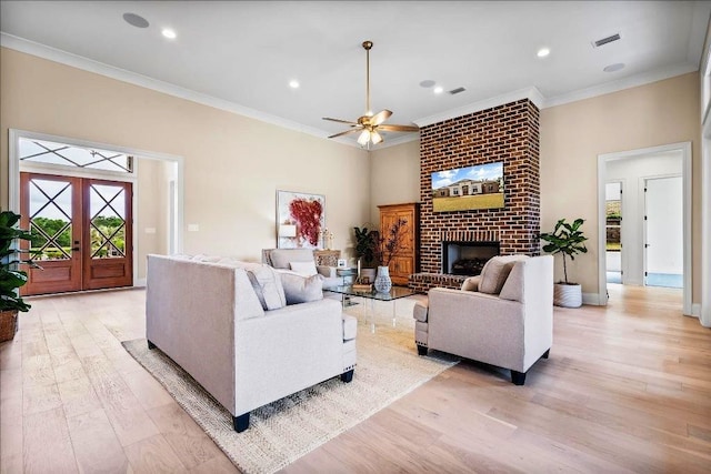 living room with french doors, a brick fireplace, ceiling fan, and light wood-type flooring