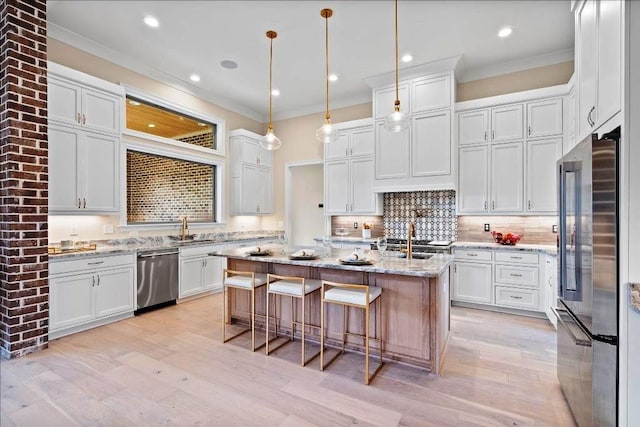 kitchen with hanging light fixtures, a kitchen island with sink, light stone countertops, appliances with stainless steel finishes, and tasteful backsplash