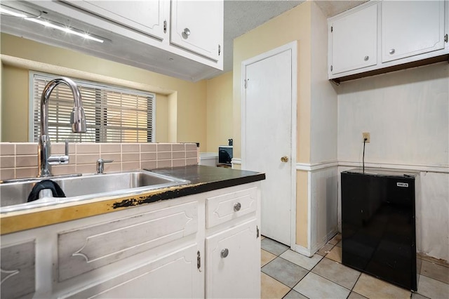 kitchen with black refrigerator, sink, white cabinets, and light tile patterned floors