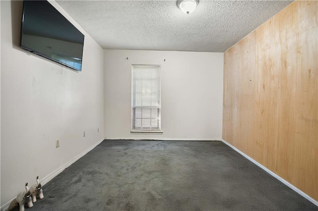 unfurnished room with wood walls, a textured ceiling, and dark carpet