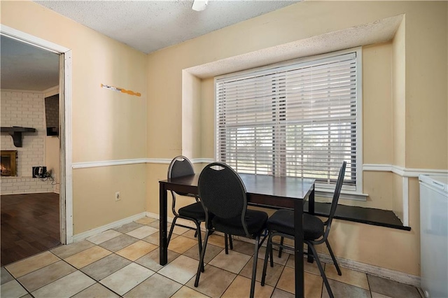 tiled dining area featuring a textured ceiling and a brick fireplace