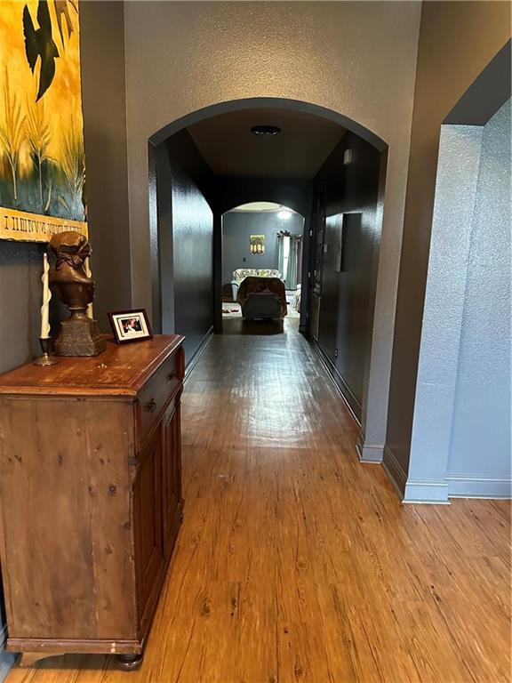 corridor featuring baseboards, arched walkways, wood finished floors, and a textured wall