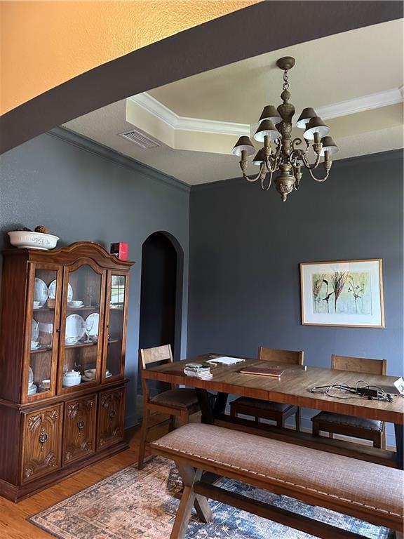 dining space featuring arched walkways, crown molding, light wood finished floors, a raised ceiling, and a chandelier