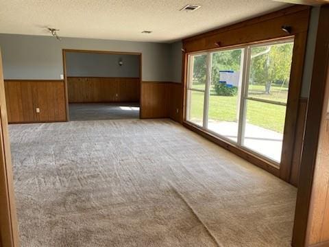 unfurnished room featuring wood walls, light colored carpet, and a textured ceiling