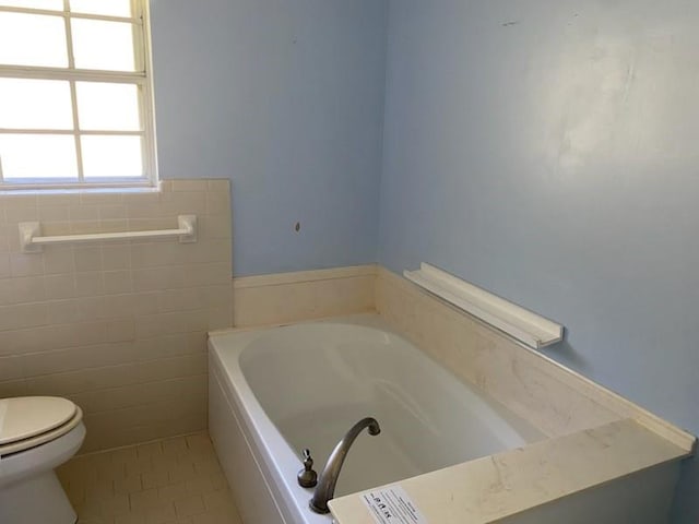 bathroom featuring a tub to relax in, tile patterned flooring, toilet, and tile walls