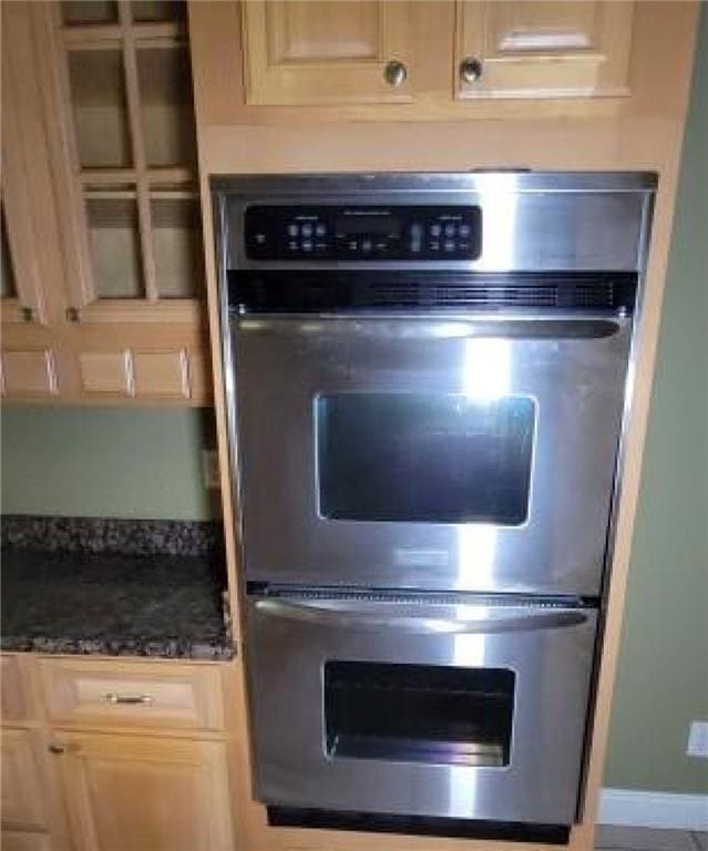 kitchen with dark stone counters, stainless steel double oven, and light brown cabinetry