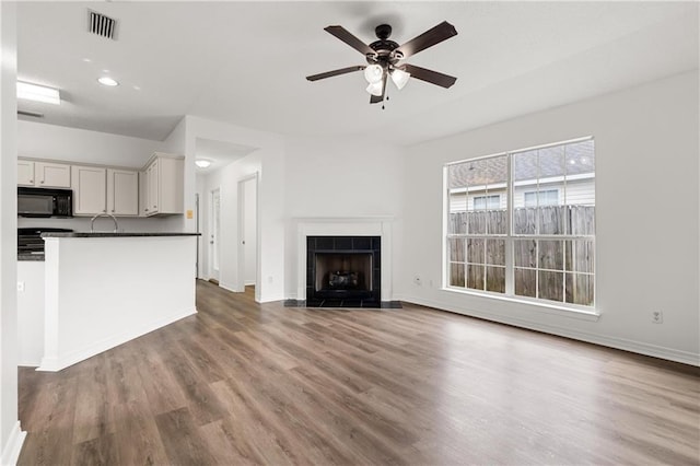 unfurnished living room featuring ceiling fan, a tiled fireplace, and hardwood / wood-style floors