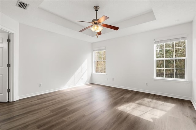 empty room featuring dark wood-type flooring, ceiling fan, and a tray ceiling