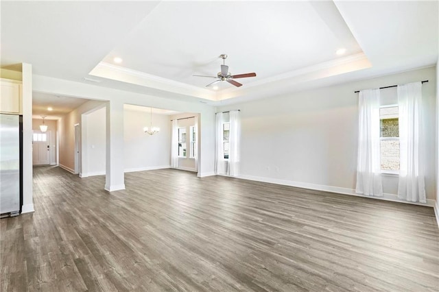 unfurnished living room with ceiling fan with notable chandelier, wood finished floors, a raised ceiling, and baseboards