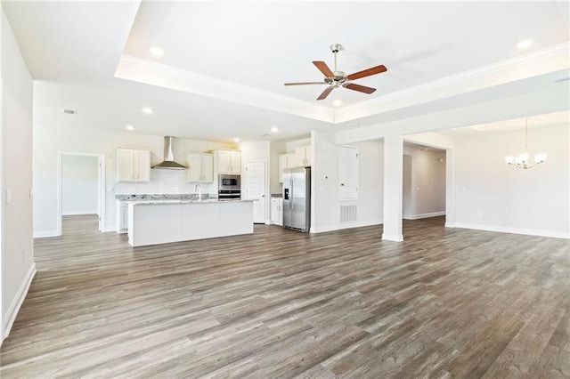 unfurnished living room with ceiling fan with notable chandelier, a sink, baseboards, light wood-style floors, and a tray ceiling