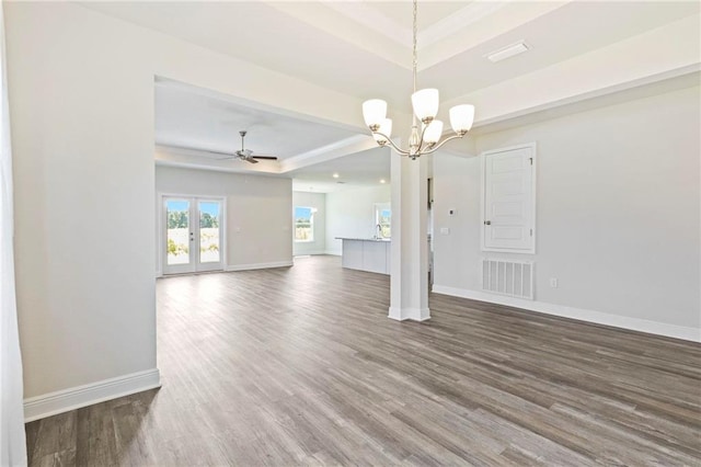 unfurnished living room featuring ceiling fan with notable chandelier, a tray ceiling, and dark hardwood / wood-style floors