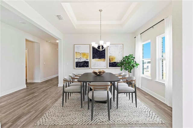 dining room with a chandelier, wood finished floors, a raised ceiling, and visible vents