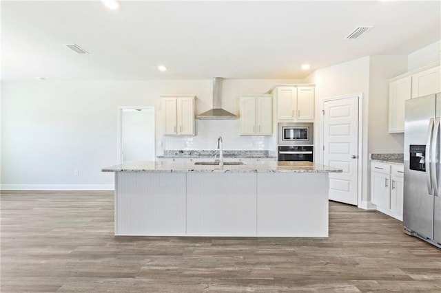 kitchen with a kitchen island with sink, wall chimney exhaust hood, appliances with stainless steel finishes, and light wood-type flooring