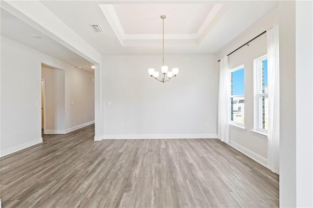 empty room with a tray ceiling, wood finished floors, visible vents, and baseboards