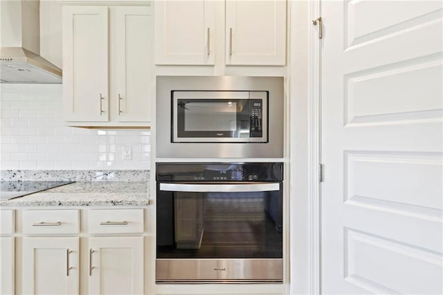 kitchen with light stone countertops, wall chimney exhaust hood, appliances with stainless steel finishes, tasteful backsplash, and white cabinetry