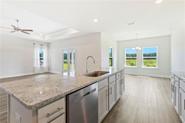 kitchen featuring dishwashing machine, light wood-type flooring, sink, a raised ceiling, and an island with sink