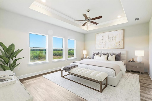 bedroom featuring wood finished floors, visible vents, baseboards, ornamental molding, and a raised ceiling