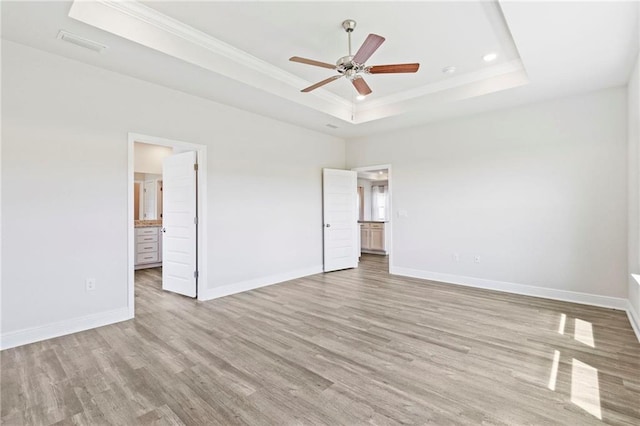 unfurnished bedroom with light wood-style floors, a tray ceiling, visible vents, and baseboards