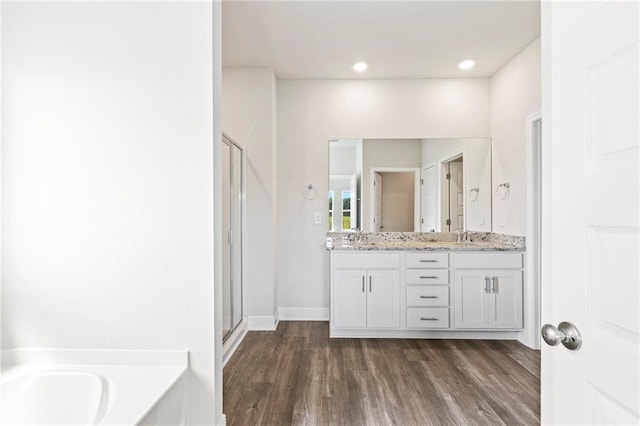 full bathroom with double vanity, a stall shower, a bath, wood finished floors, and a sink