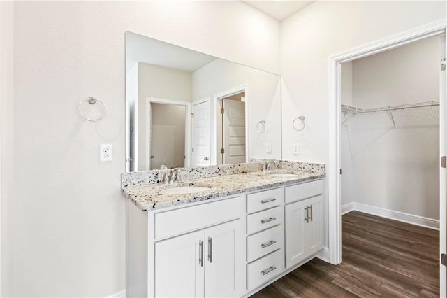 full bathroom featuring double vanity, a walk in closet, a sink, and wood finished floors