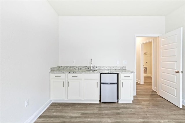 kitchen featuring freestanding refrigerator, white cabinets, and light stone countertops