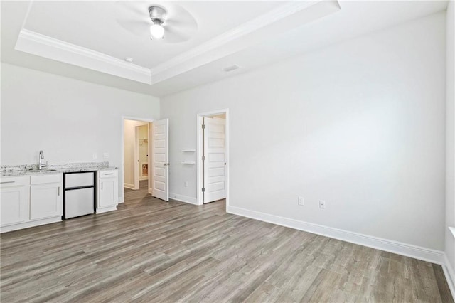 unfurnished room with light wood finished floors, baseboards, ornamental molding, a tray ceiling, and a sink