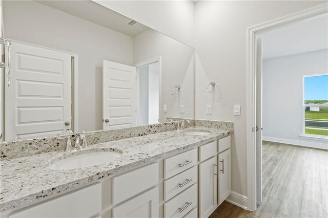 full bath featuring double vanity, a sink, baseboards, and wood finished floors