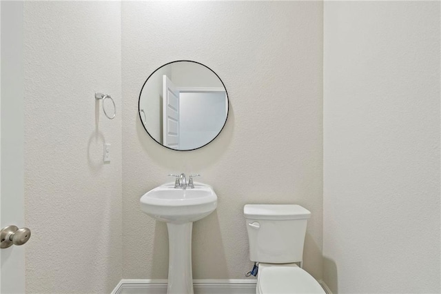 half bath featuring baseboards and toilet