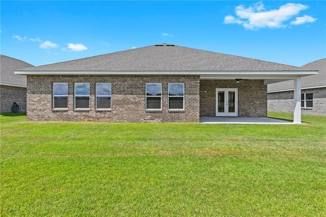 back of property with french doors, brick siding, a lawn, and roof with shingles