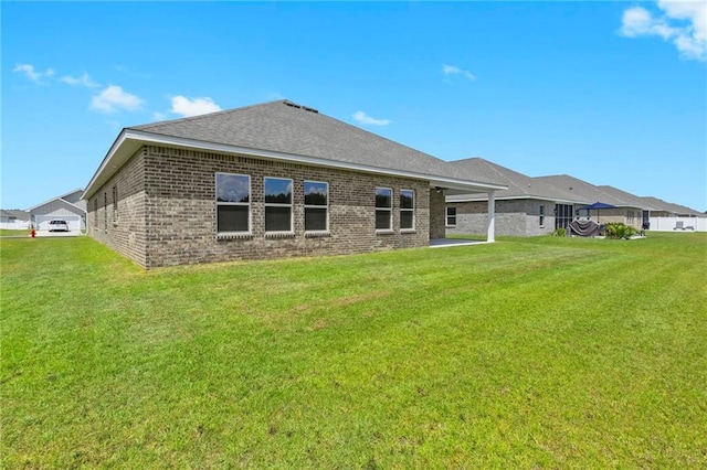 rear view of property featuring roof with shingles, a lawn, and brick siding