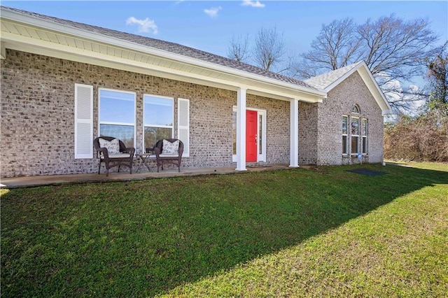 view of exterior entry with brick siding, a yard, and a patio