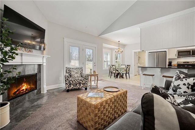 living area with an inviting chandelier, baseboards, high vaulted ceiling, and a tile fireplace