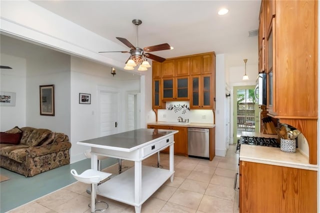 kitchen with glass insert cabinets, a ceiling fan, brown cabinetry, light countertops, and appliances with stainless steel finishes