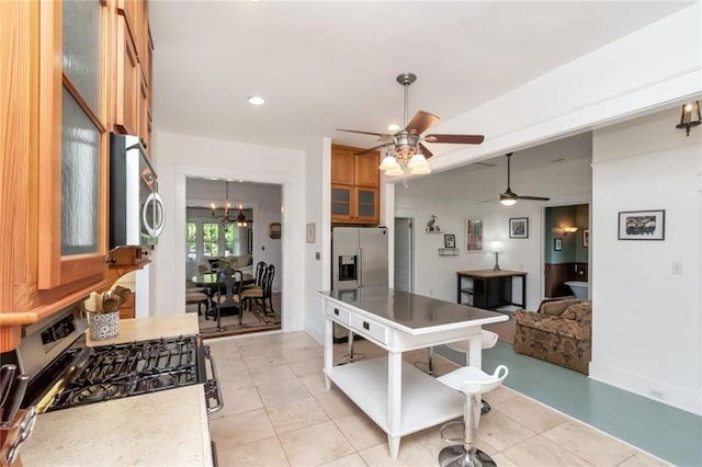 kitchen featuring pendant lighting, glass insert cabinets, ceiling fan with notable chandelier, brown cabinets, and stainless steel appliances