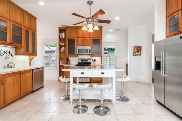 kitchen with brown cabinets, a breakfast bar, a sink, stainless steel appliances, and ceiling fan