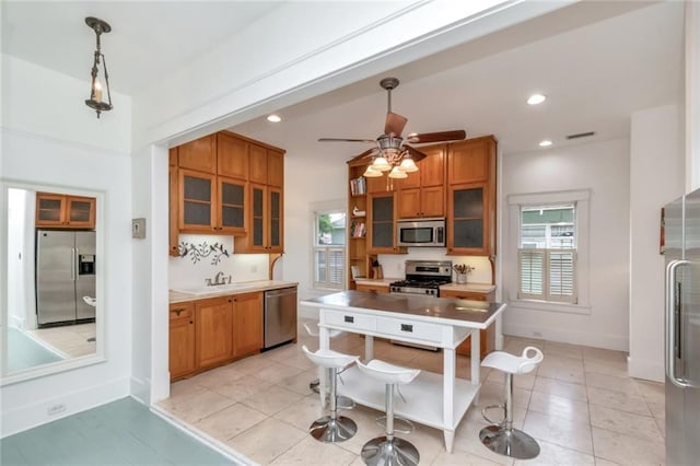kitchen with glass insert cabinets, stainless steel appliances, brown cabinetry, and a healthy amount of sunlight