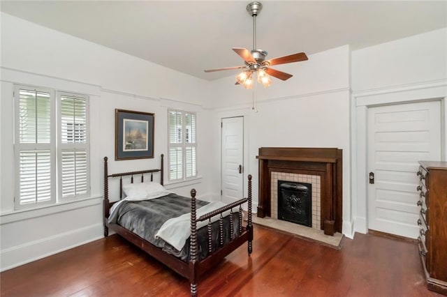 bedroom featuring ceiling fan, a tile fireplace, baseboards, and wood finished floors