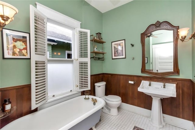 full bathroom featuring toilet, a wainscoted wall, wooden walls, a ceiling fan, and a freestanding tub
