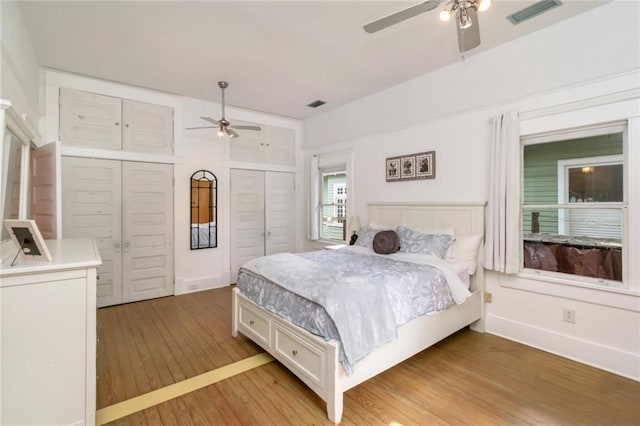 bedroom featuring ceiling fan, light wood-style flooring, visible vents, and two closets