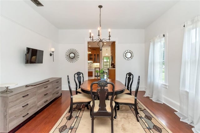 dining space featuring a chandelier, wood finished floors, baseboards, and visible vents