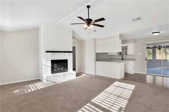 unfurnished living room featuring lofted ceiling with beams, ceiling fan, a brick fireplace, and dark carpet